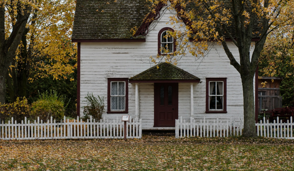White clapboard house with burgundy trim and white picket fence surrounded by golden autumn leaves in an Ohio neighborhood